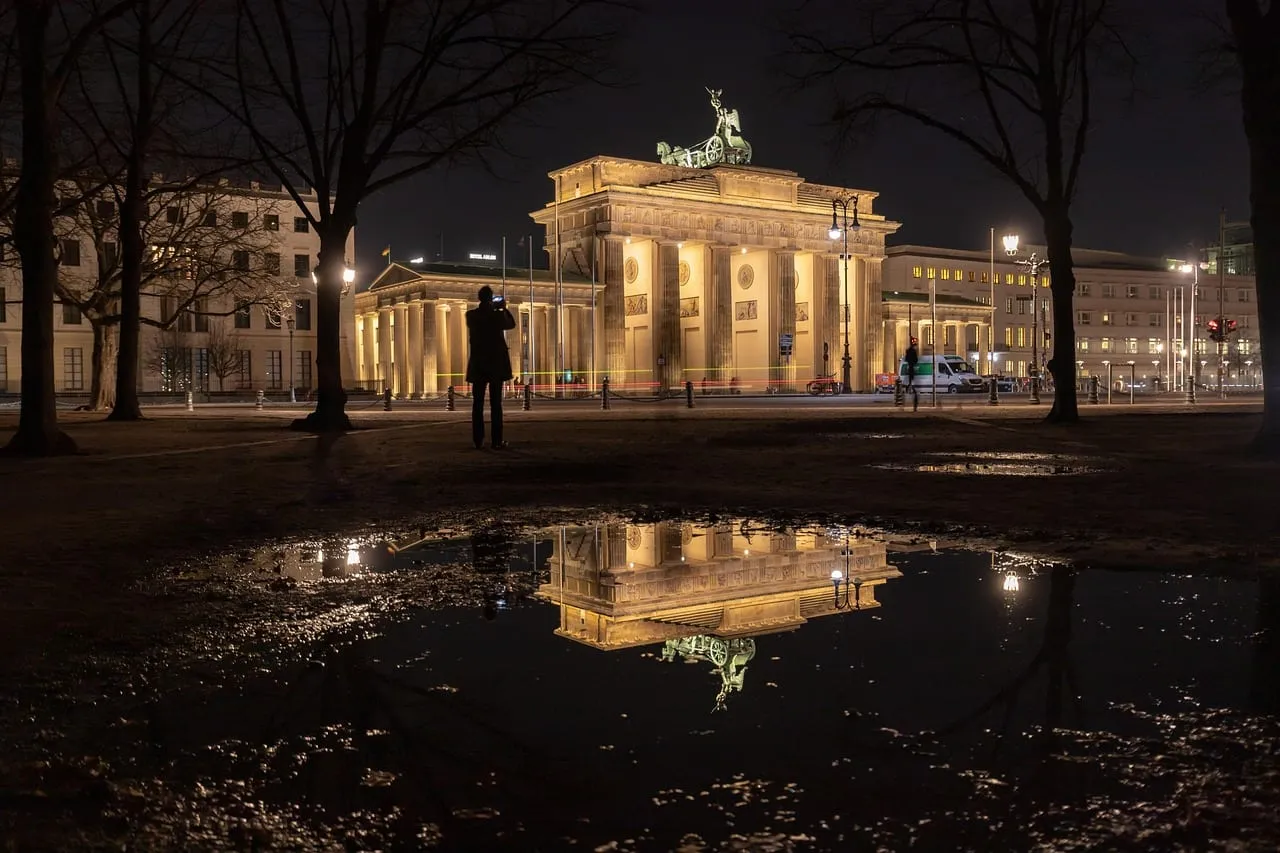 La porte de Brandebourg illuminée la nuit, reflétée dans une flaque