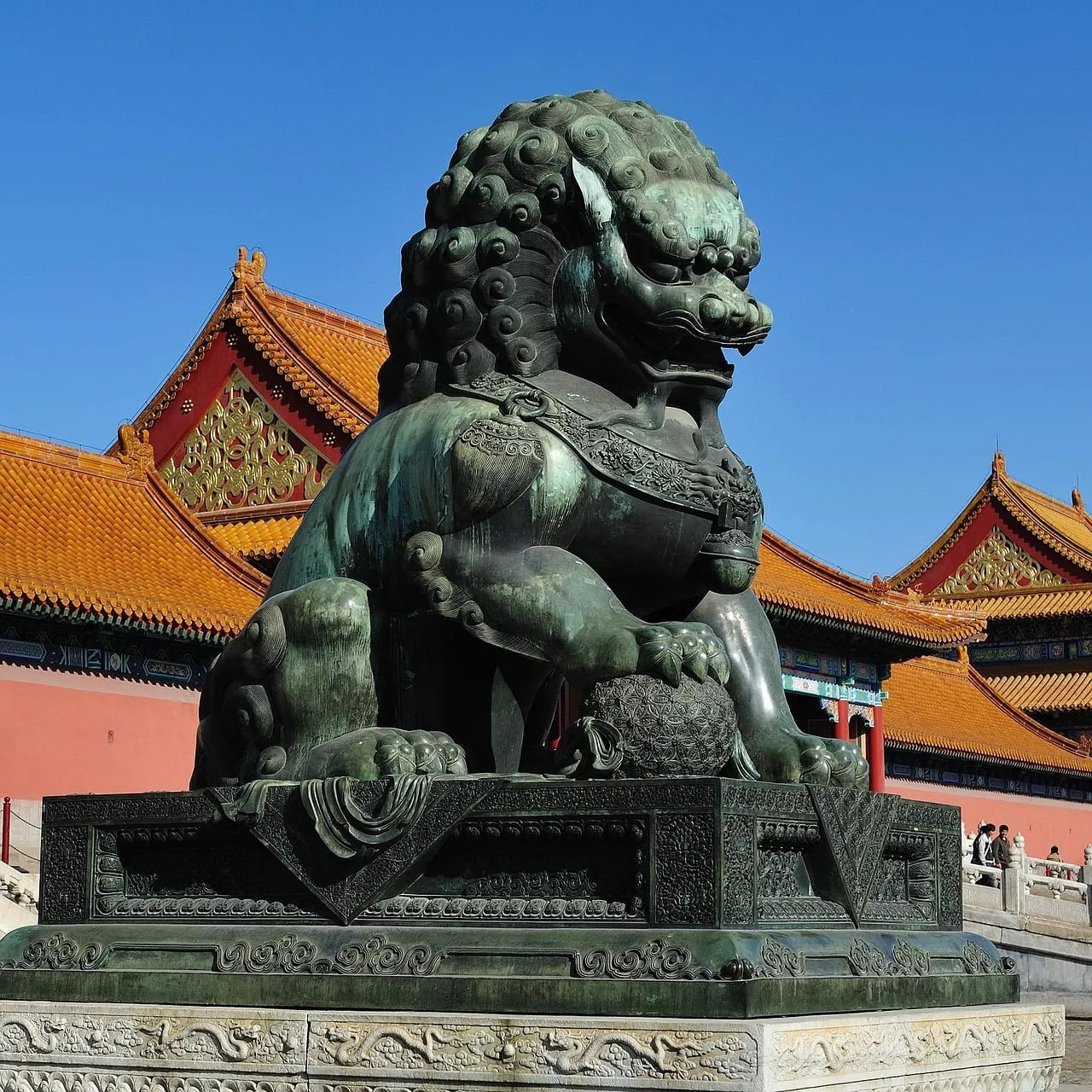 Un lion gardien en bronze devant des murs rouges et des toits jaunes