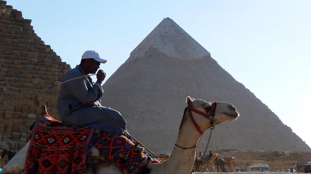 Un chamelier qui se repose à côté d’une pyramide